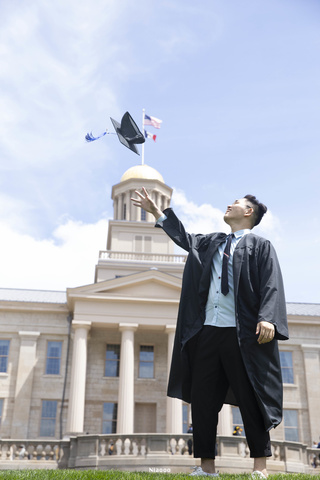 student throwing graduation hat in air in front of Old Capitol