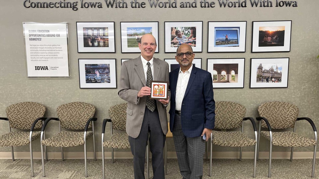 Russell Ganim with Anant Chakradeo in front of International Programs photos and "connecting Iowa with the world and the world with Iowa"