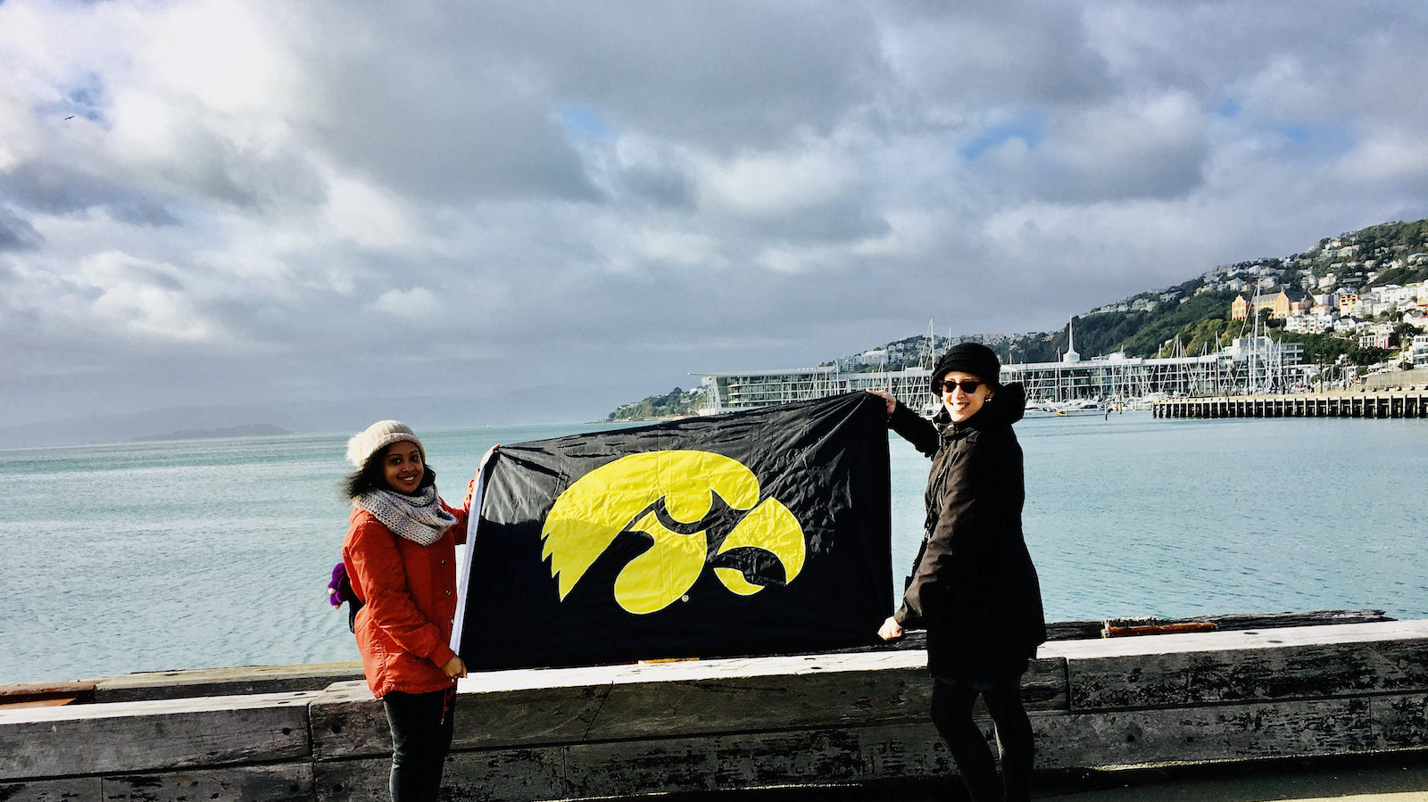 photo of Iowa students holding a University of Iowa flag on the waterfront in New Zealand.