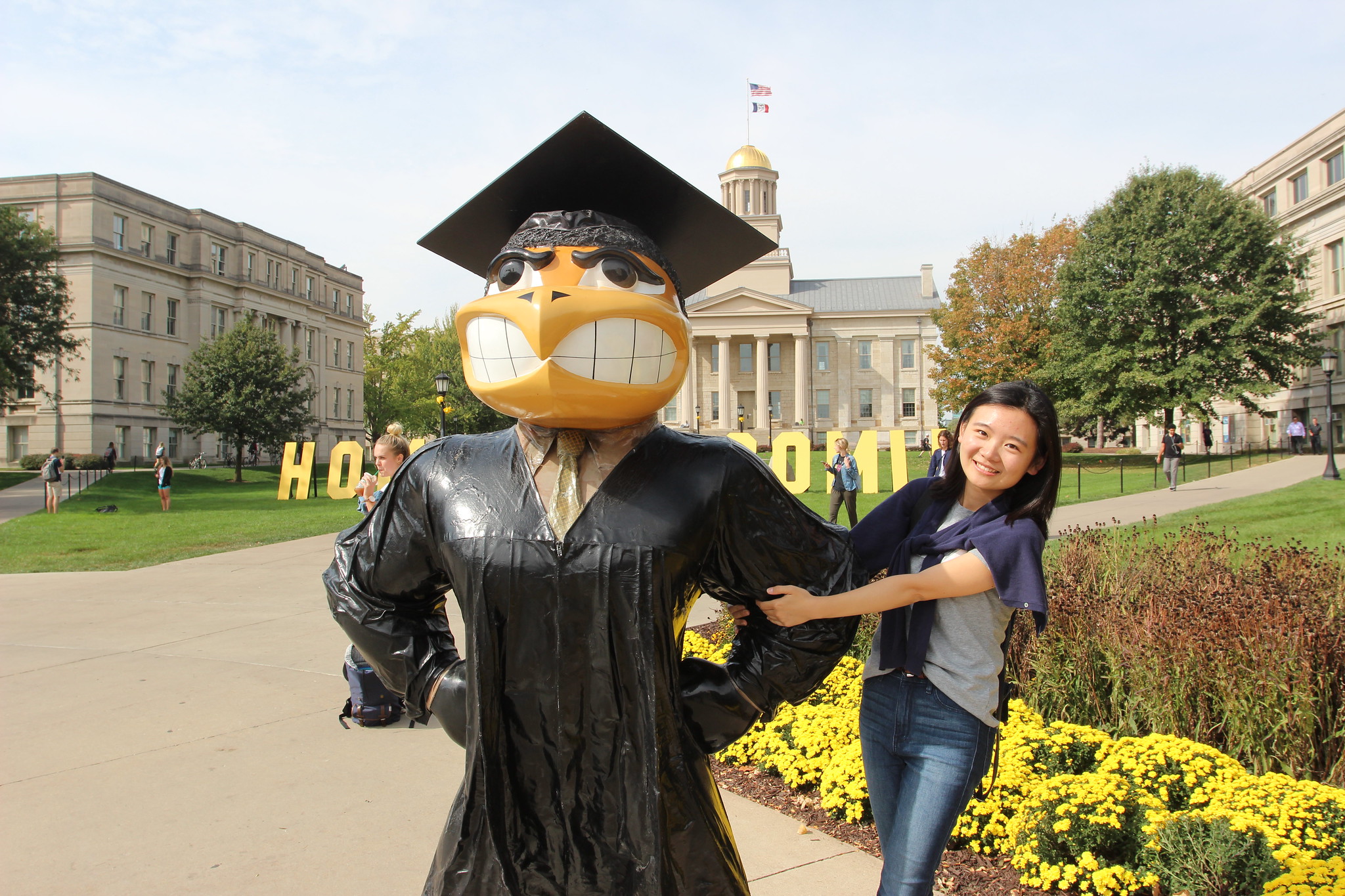 international student holding on to graduating herky statue