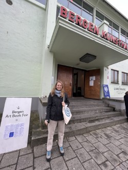 Kathleen Maris Paltrineri outside next to a sign that reads "Bergen Art Book Fair"