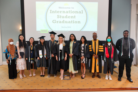 students standing in front of projector that says International Student Graduation