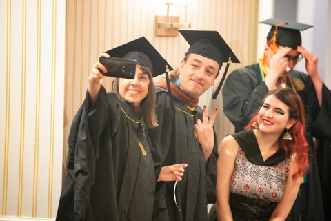 students wearing graduation regalia taking selfie at graduation celebration