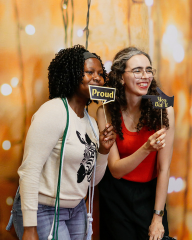 Jane & Mariana, two international students, smiling holding signs in a photo booth at an international student end-of-year event.