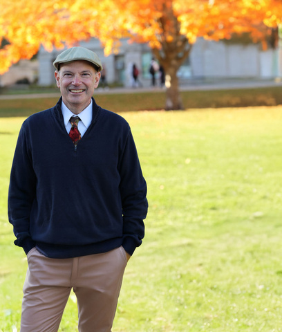 Russ Ganim with hands in pocket smiling in front of fall scene on campus