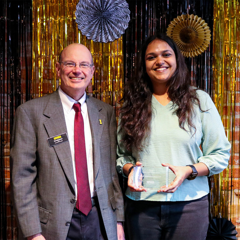 dean and student hold glass award in front of black and gold backdrop