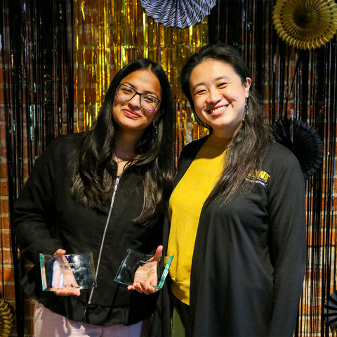 students and faculty smile for photo black and gold backdrop