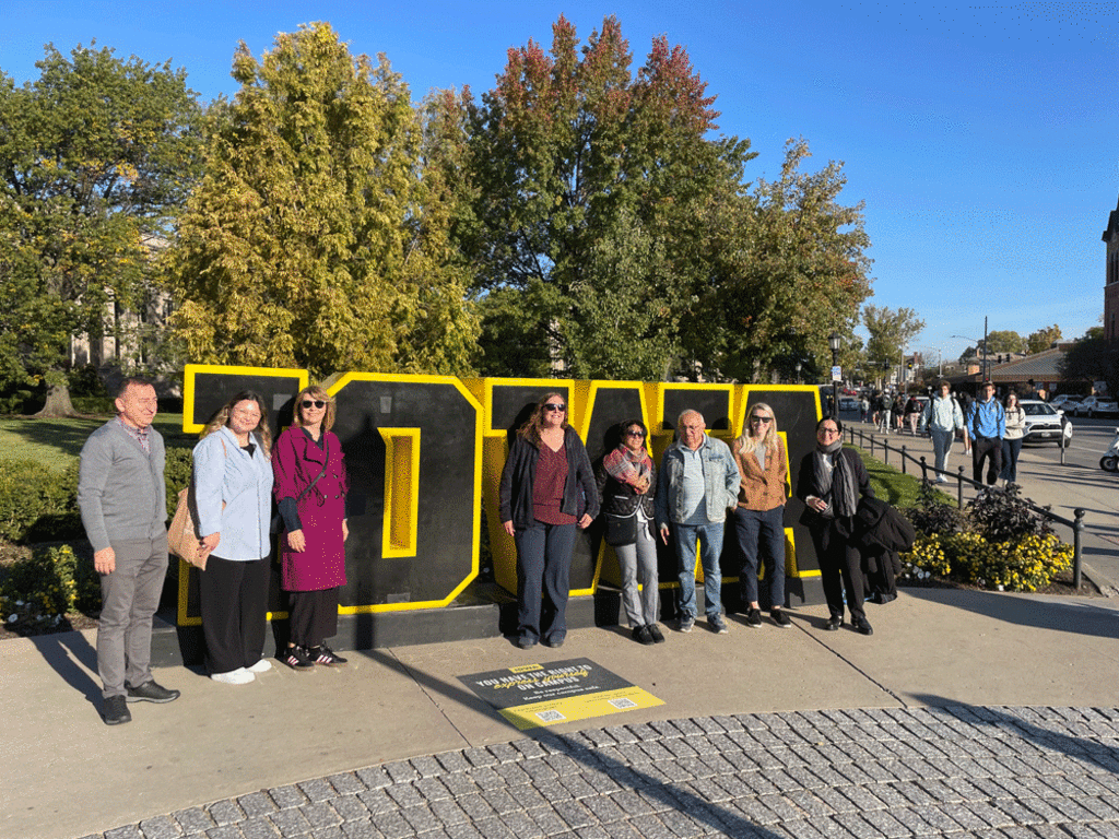 Visiting delegation from Romania standing in front of large black and gold IOWA sign