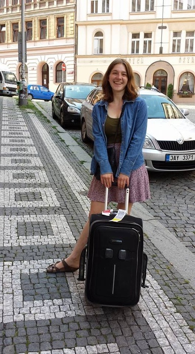 student standing on cobblestone street with suitcase