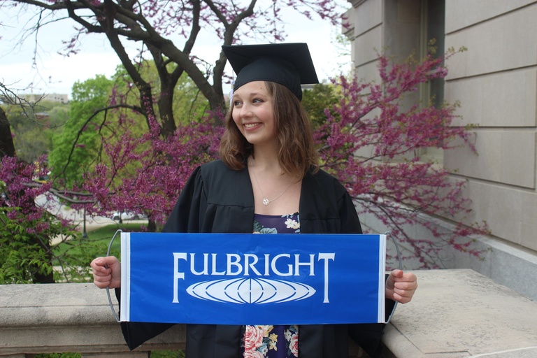 Sylvia Dean holding Fulbright flag in graduation dress