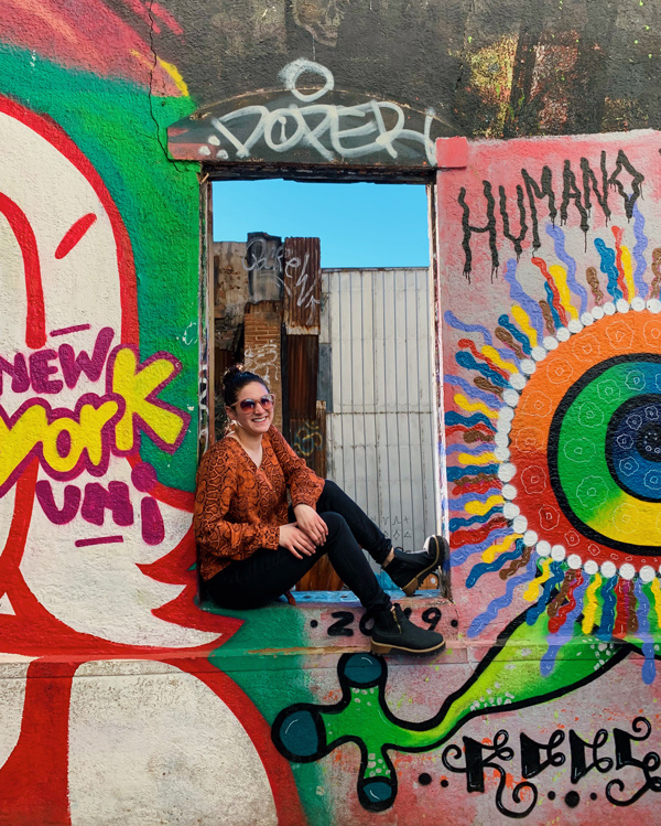 Abby Brickley sitting on wall covered in colorful grafiti