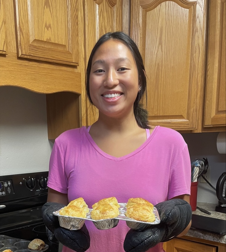 student in kitchen holding muffin tin