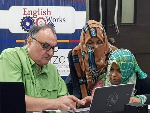 John Achrazoglou in Pakistan on laptop with Pakistani women looking on