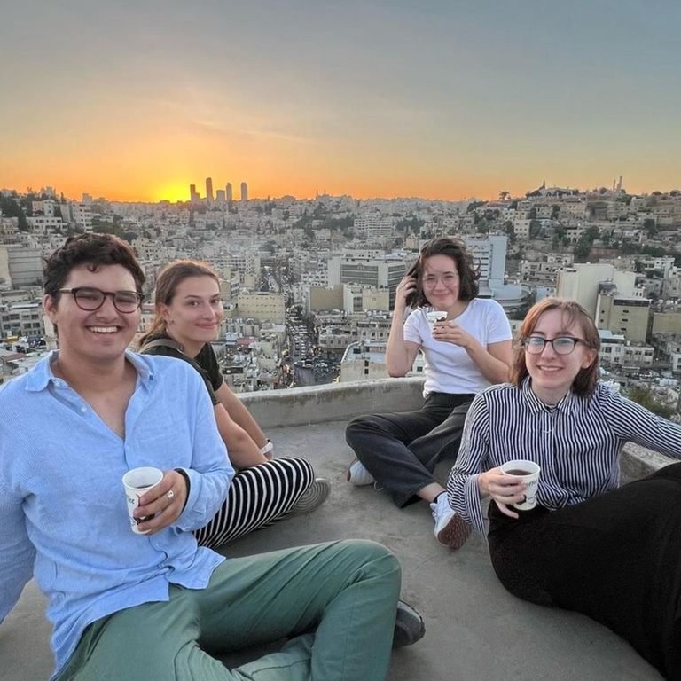 four students drinking coffee with cityscape behind them 