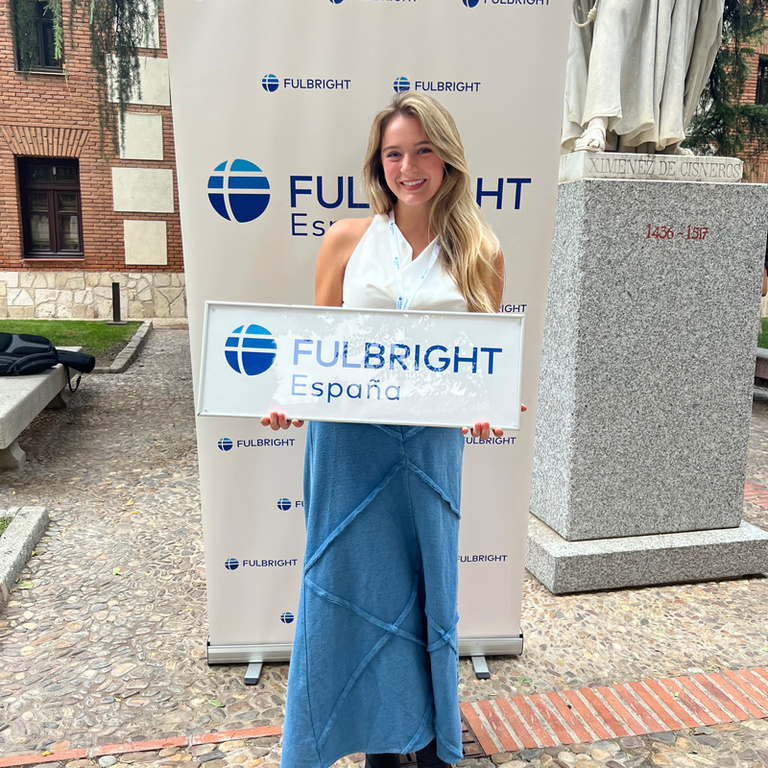 student in blue dress holding Fulbright sign