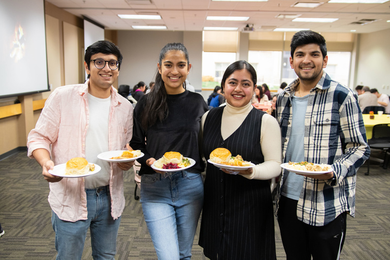 four students standing together holding plates of food