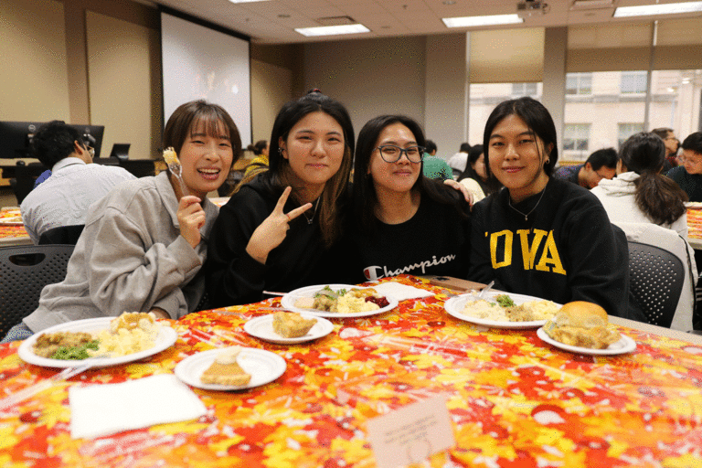 four students, one in Iowa gear, smiling at camera