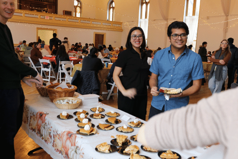 two students next to dessert table smiling