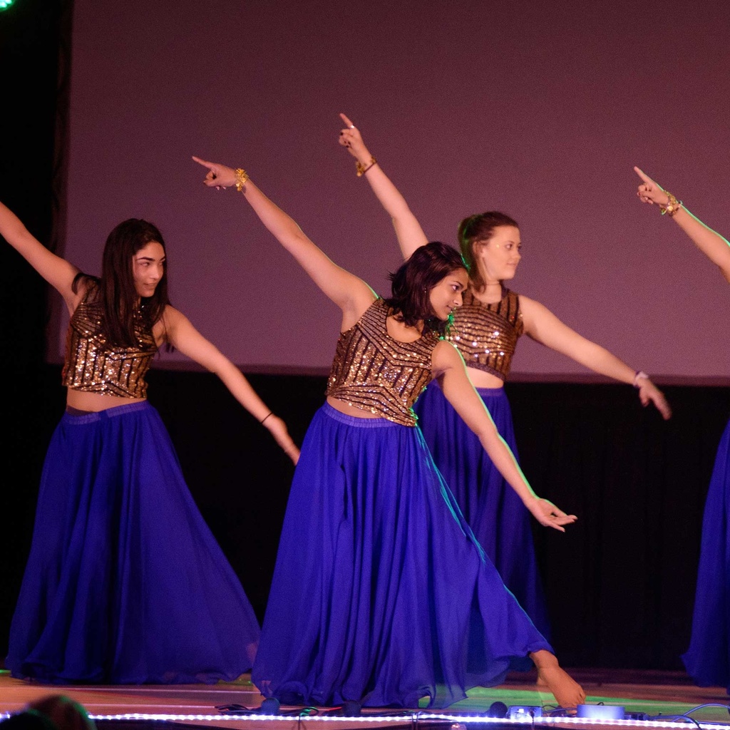 four students in blue dancing on a stage at multi-culture night
