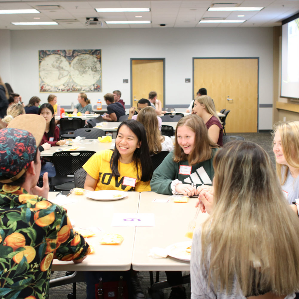 Student with Iowa shirt sitting at table with other students smiling