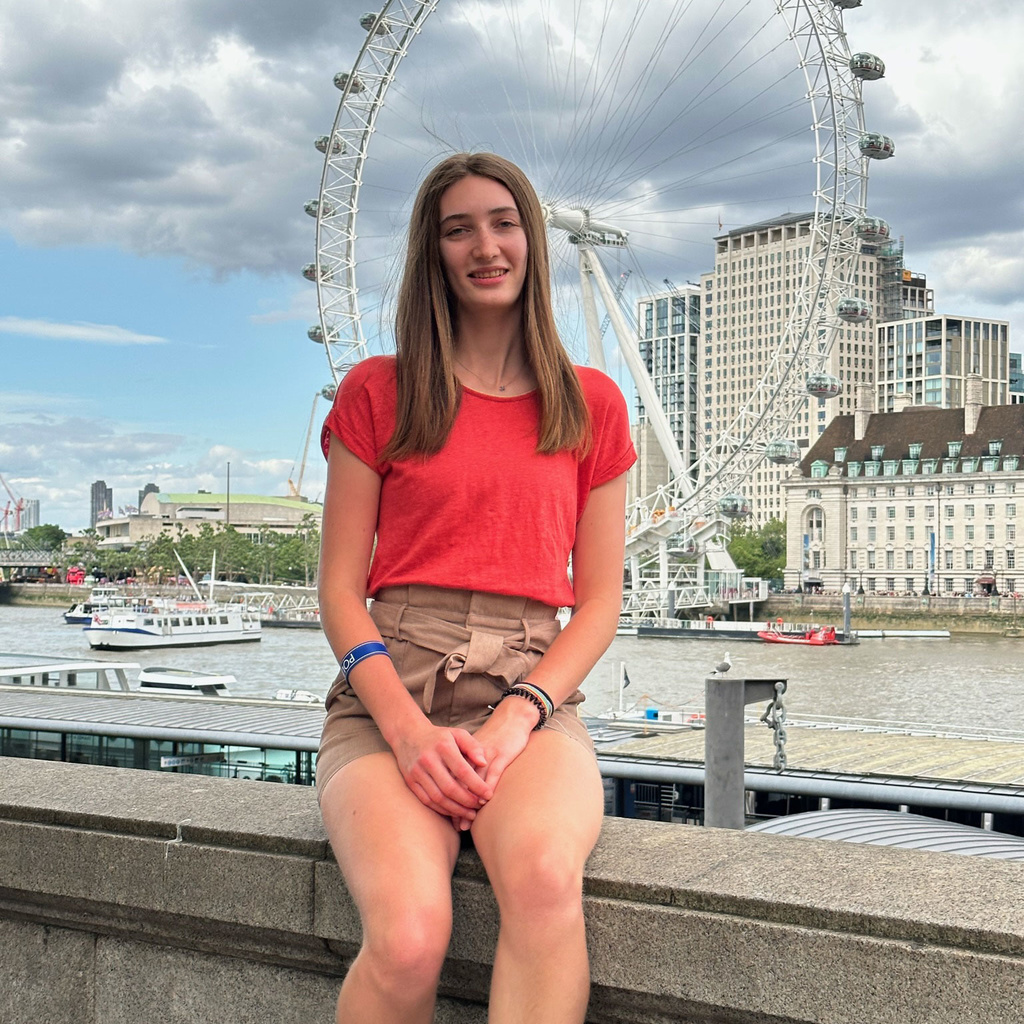 Maddie Phillips sitting in front of Ferris wheel in London