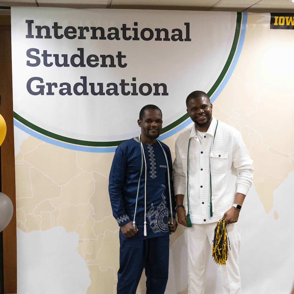 two students standing in front of a sign that says International Student Graduation Celebration, having their photo taken