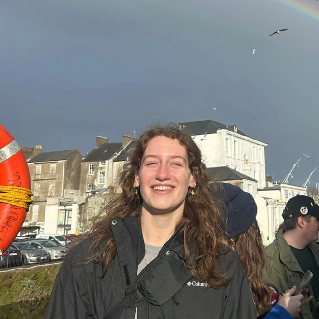 Jennifer Schmitt standing in front of rainbow and buildings and seagulls in the sky