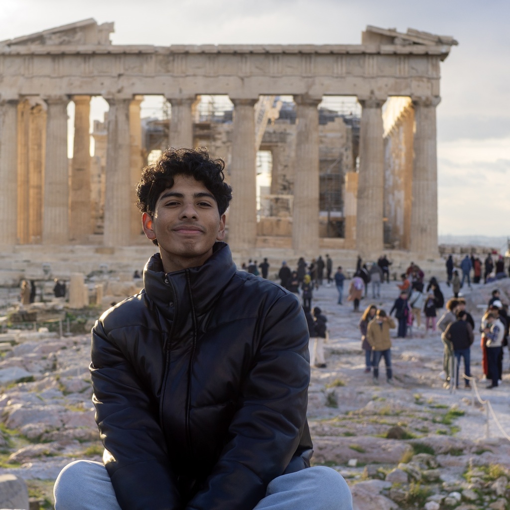 student sitting in front of ancient Greek temple smiling