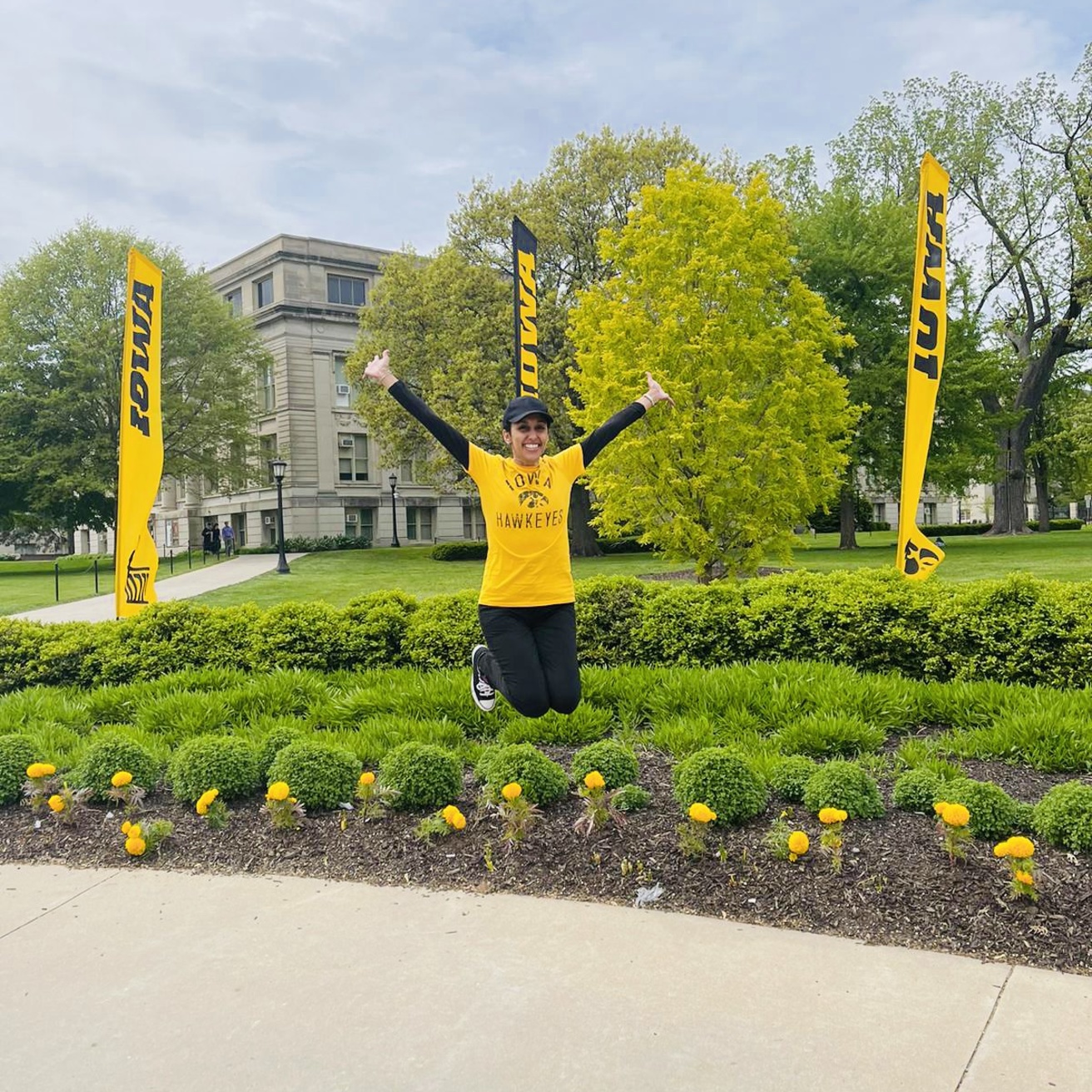 Demah AlGheithy jumping for joy on graduation day in front of UI flags