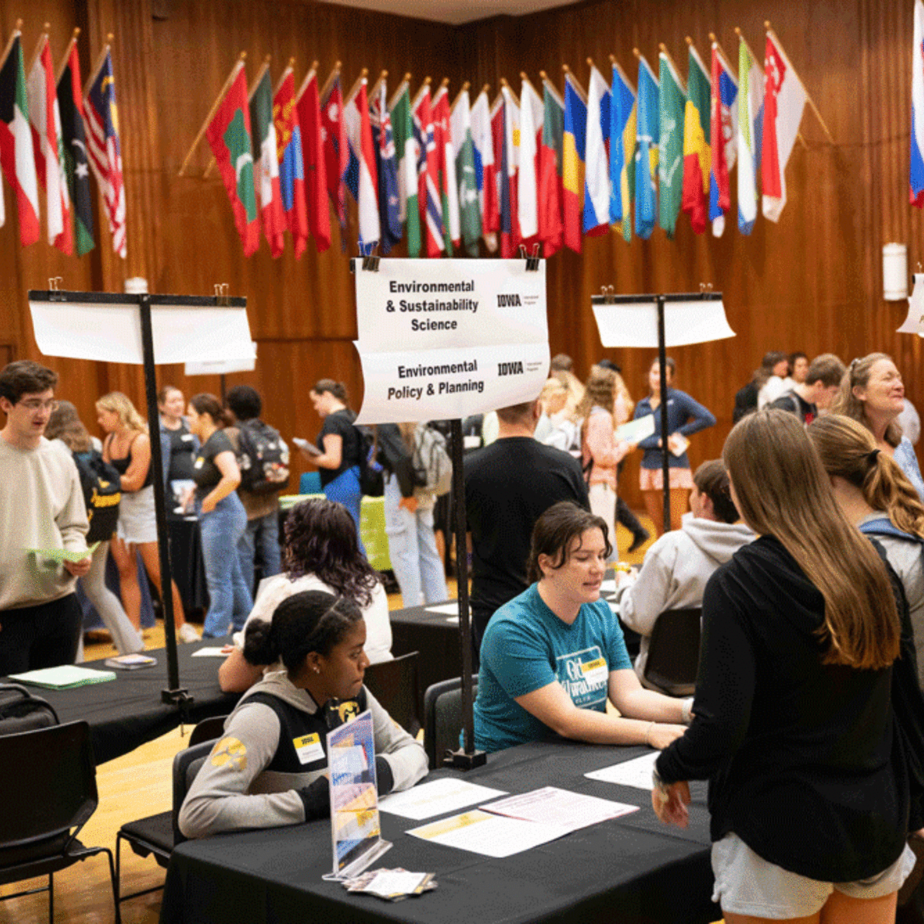 students talking with people at Environmental and Sustainability Science table in room with international flags 