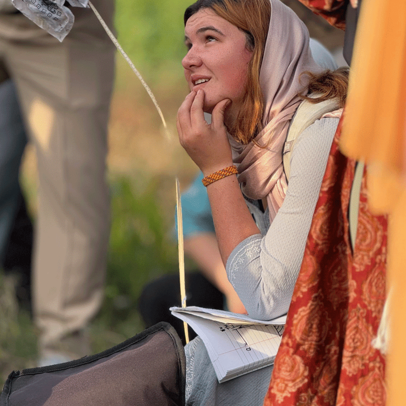 student crouching down in grass listening in traditional Indian dress