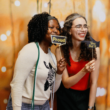 two students holding signs - proud, you did it - for photo