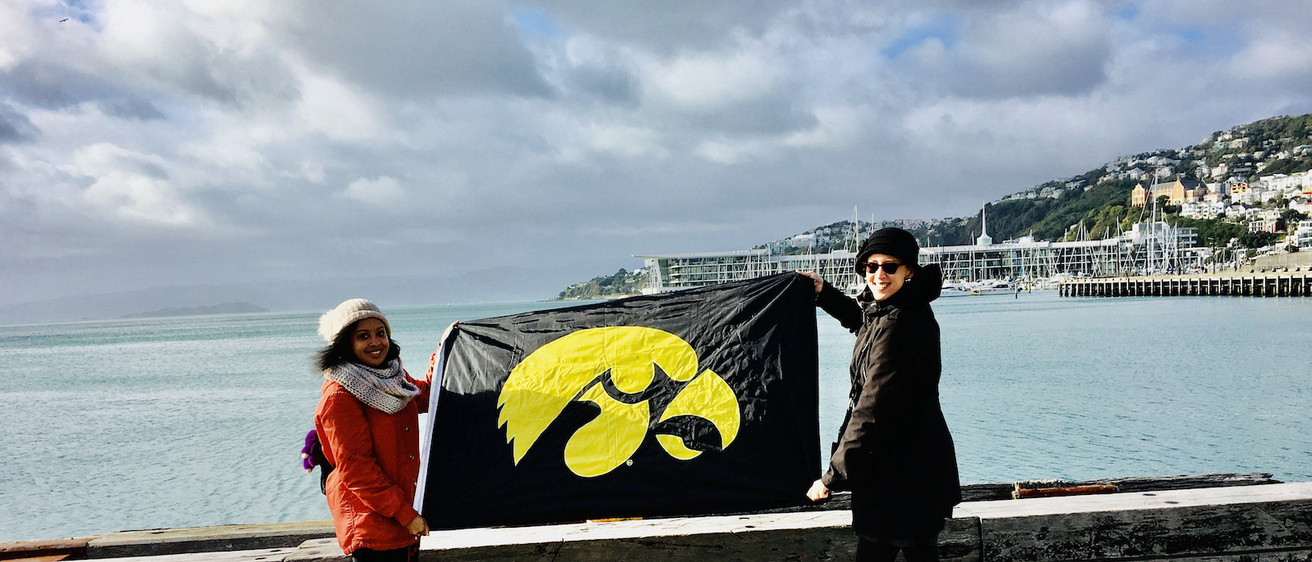 photo of Iowa students holding a University of Iowa flag on the waterfront in New Zealand.