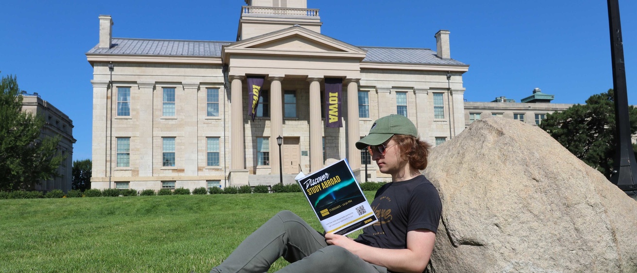 Sam Waldron reading study abroad brochure sitting against rock in front of old capitol