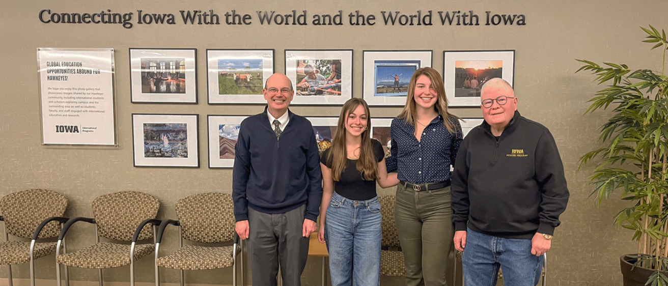 Russ Ganim, Samantha Hitlan, Peyton Pangburn, and Dick Tyner in front of images and "Connecting Iowa with the World and the World with Iowa"