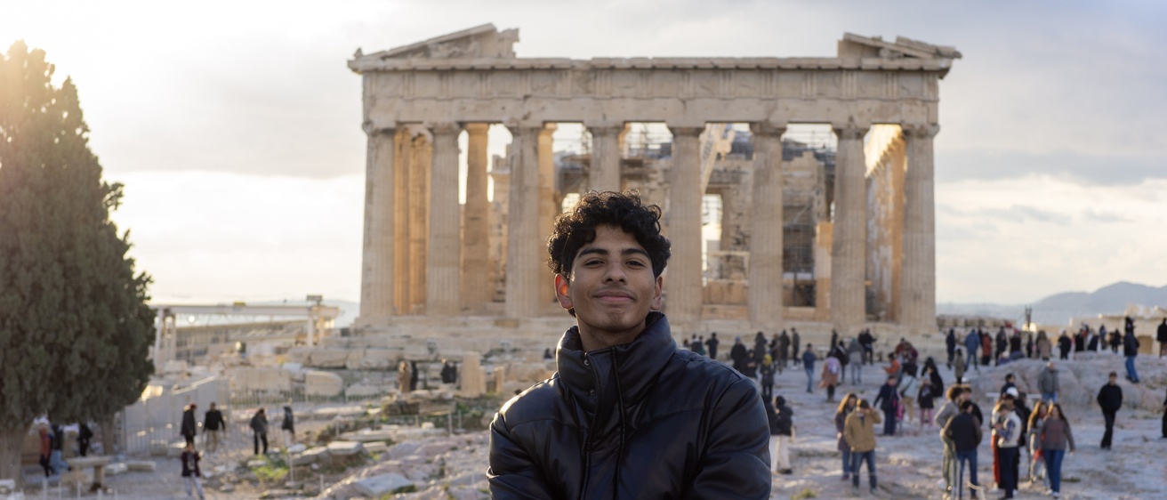student sitting in front of ancient Greek temple smiling