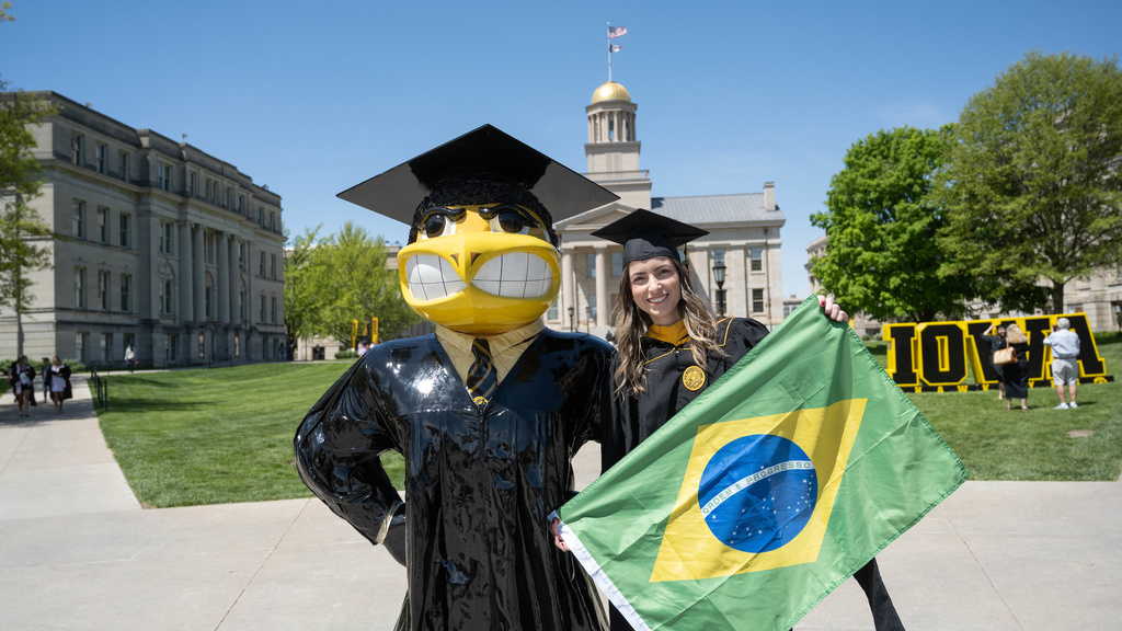 Student holding Brazilian flag next to graduate herky by Old Capitol