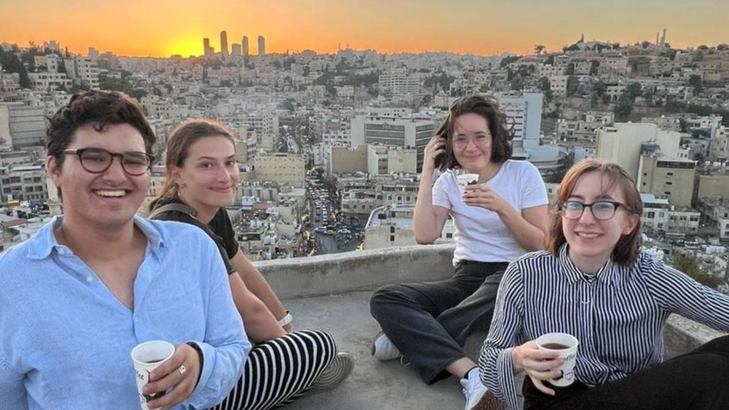 four students drinking coffee with cityscape behind them 