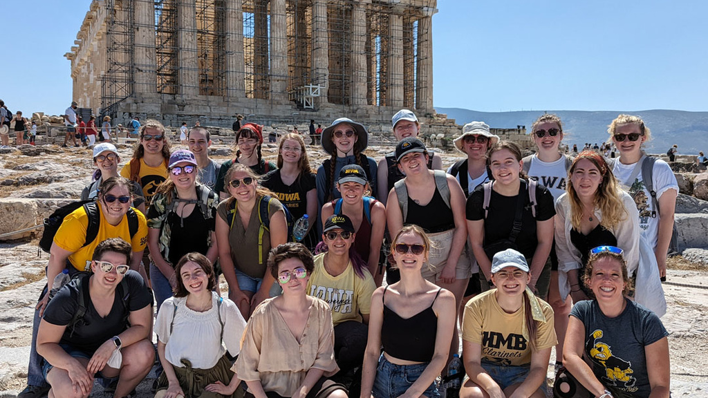 group of students kneeling in front of ancient ruins
