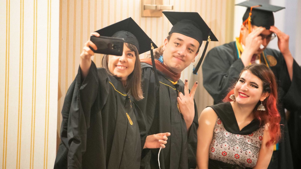 students wearing graduation regalia taking selfie at graduation celebration