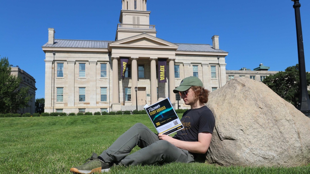 Sam Waldron reading study abroad brochure sitting against rock in front of old capitol