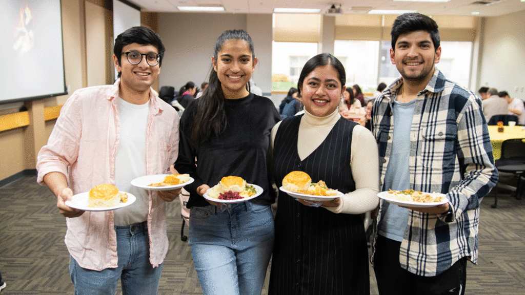 four students smiling holding plates of Thanksgiving food