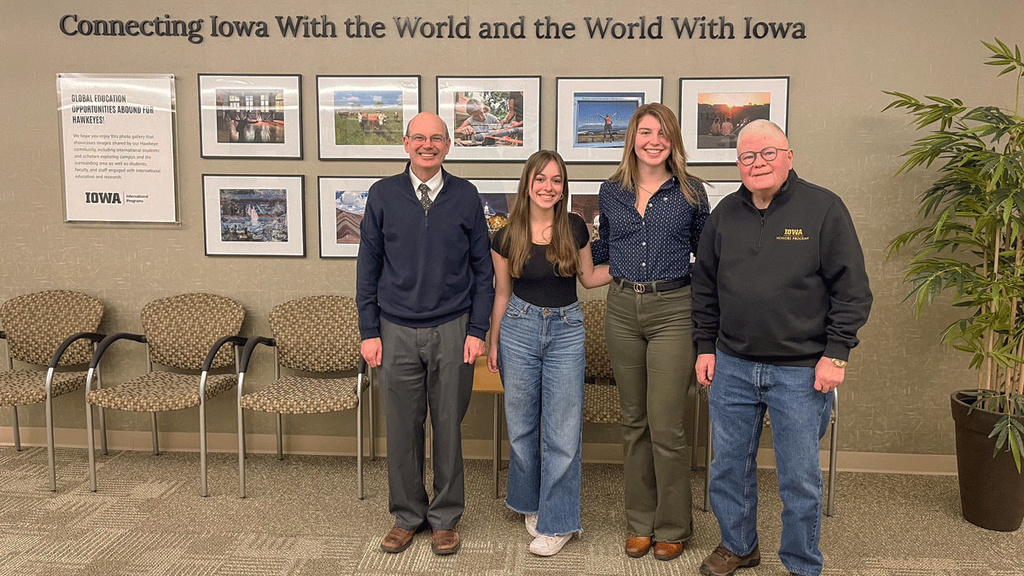 Russ Ganim, Samantha Hitlan, Peyton Pangburn, and Dick Tyner in front of images and "Connecting Iowa with the World and the World with Iowa"