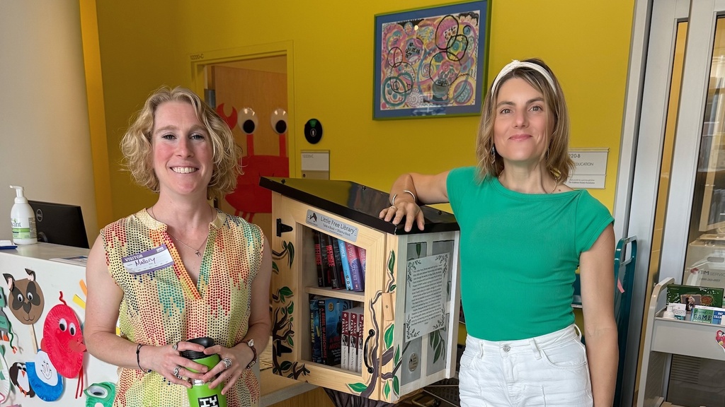 two directors in colorful tops leaning on the Little Free Library box, yellow background