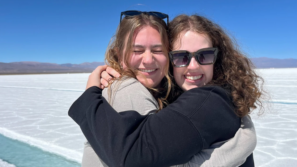 Two students hugging on white beach with blue water stream