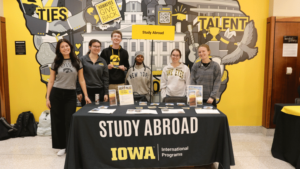 students standing around table with Study Abroad on it, State of Iowa with Hawkeye colors and images behind them