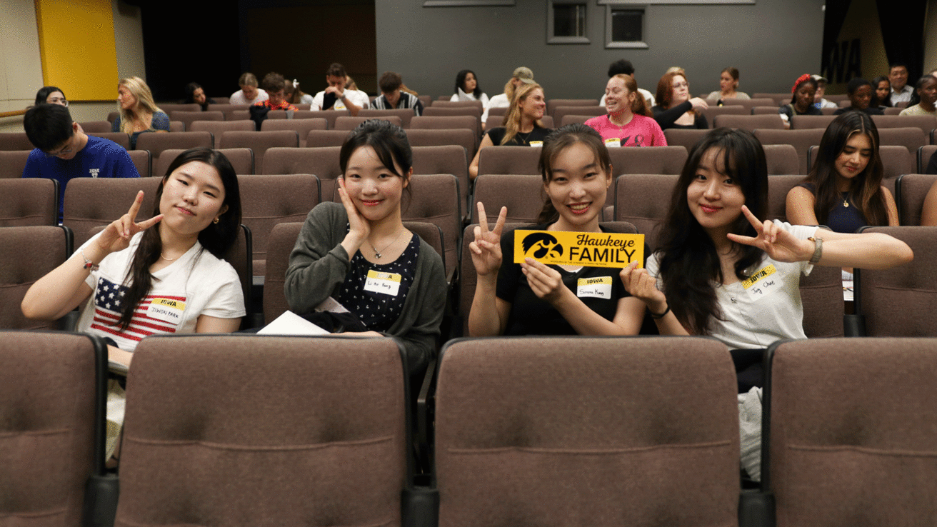 international students sitting down holding Hawkeye Family sticker